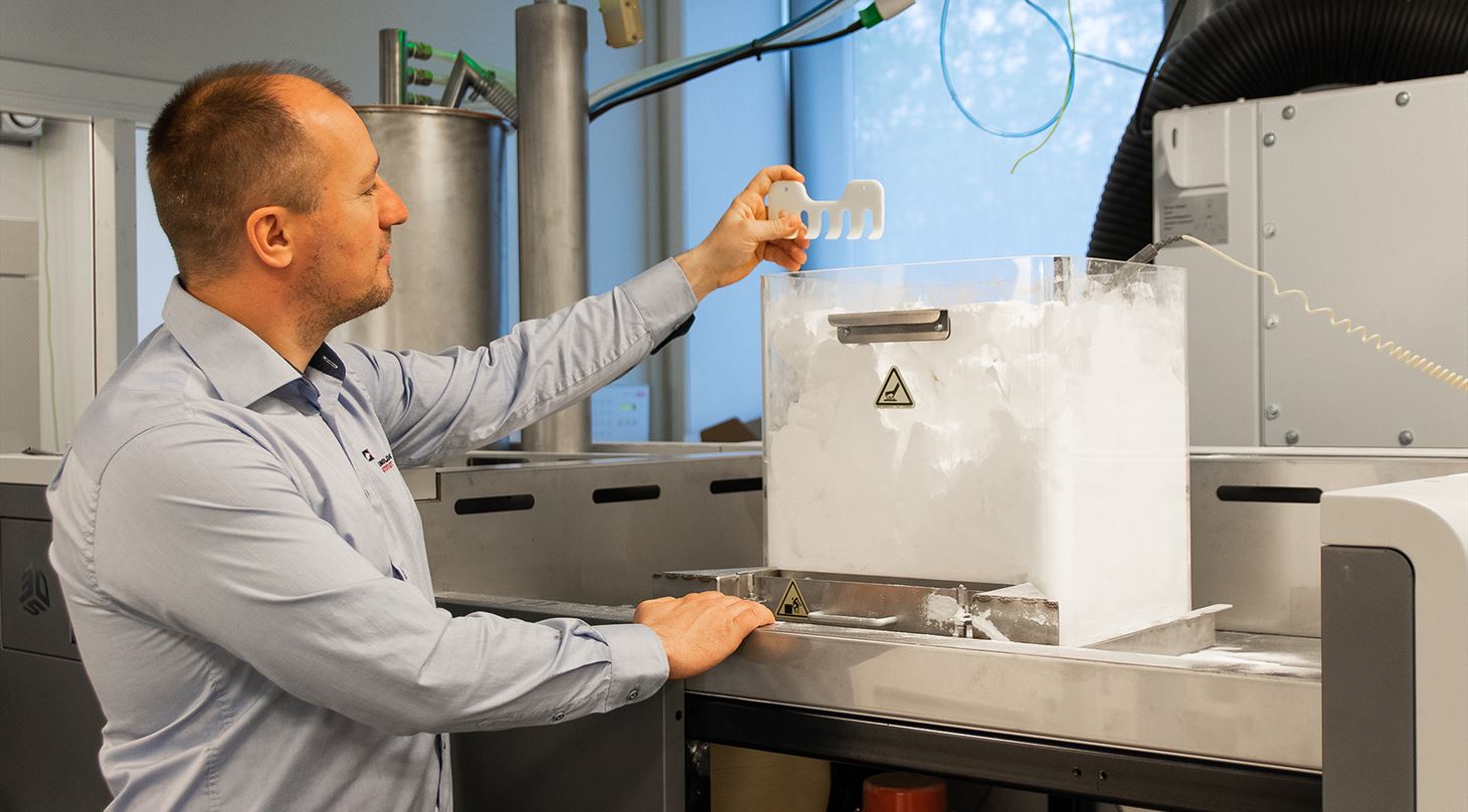 Mand foran 3D-printer med emne i hånden